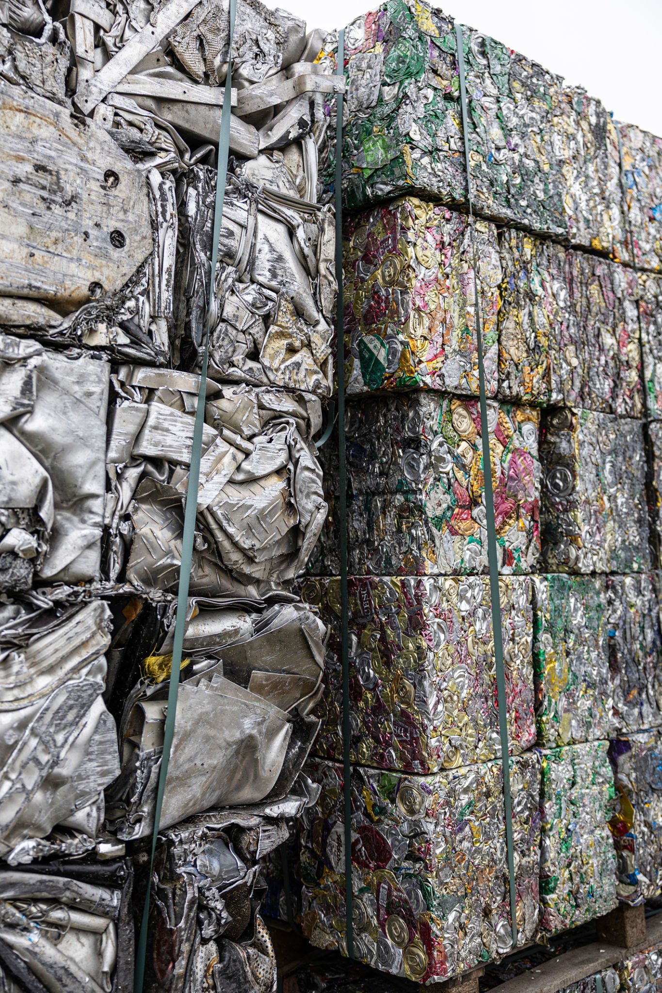 Industrial piles of compressed scrap metal and colorful aluminum cans bundled in blocks, ready for recycling and reuse